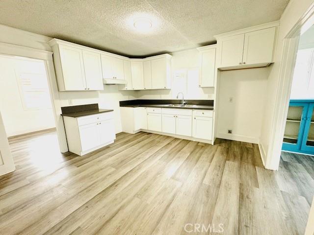 kitchen featuring light wood finished floors, dark countertops, a sink, and white cabinets