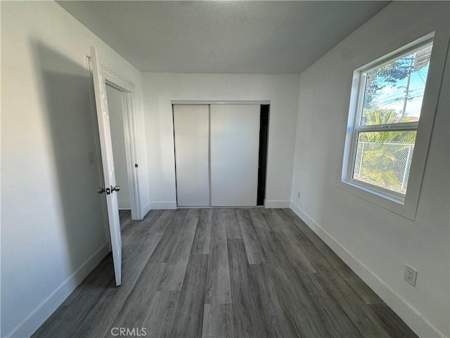 unfurnished bedroom with dark wood-style floors, a closet, and baseboards