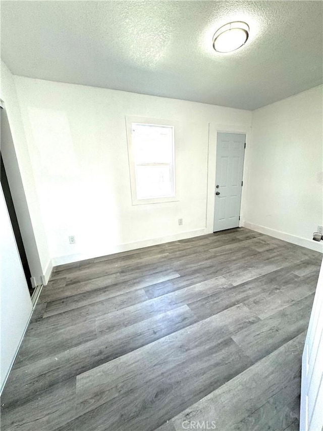 unfurnished room featuring a textured ceiling, dark wood-type flooring, and baseboards