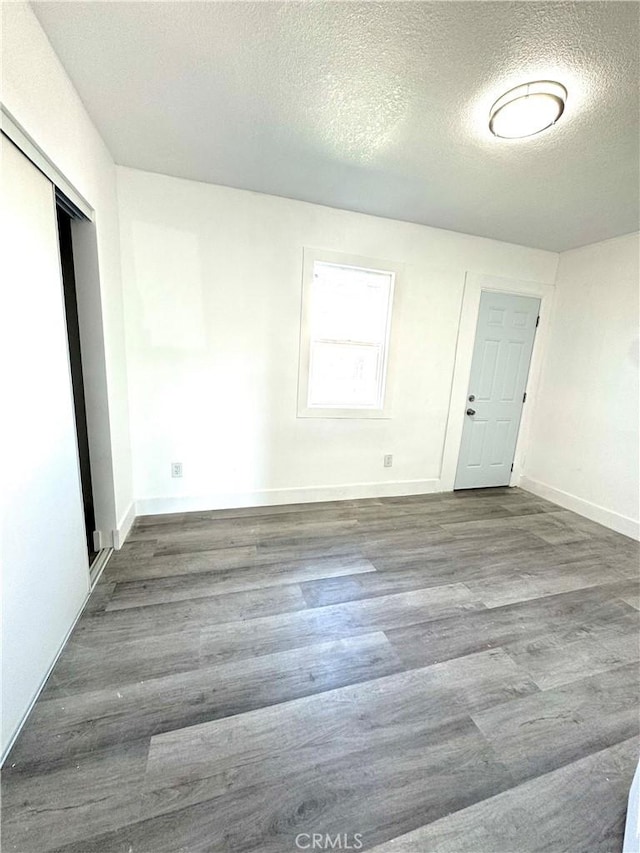 empty room featuring a textured ceiling, baseboards, and wood finished floors