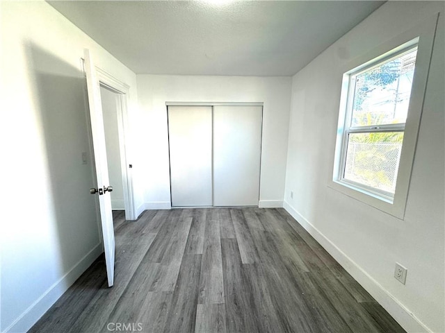 unfurnished bedroom with dark wood-type flooring, a closet, and baseboards