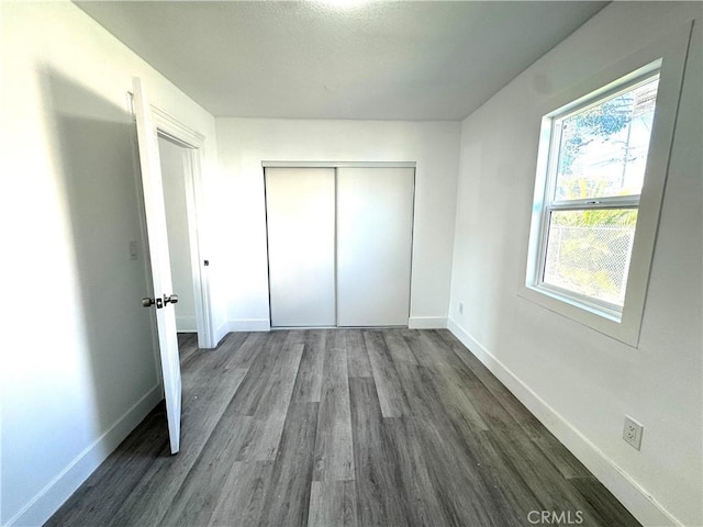 unfurnished bedroom featuring dark wood-type flooring, a closet, and baseboards