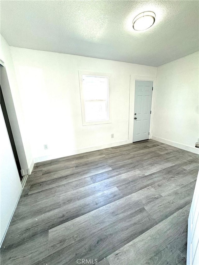 empty room with dark wood-style floors, a textured ceiling, and baseboards