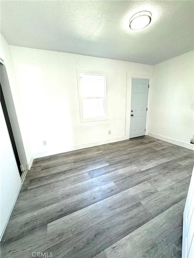 spare room with a textured ceiling, wood finished floors, and baseboards