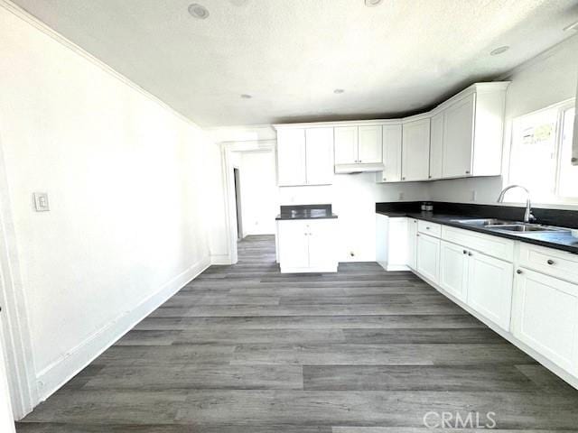 kitchen with baseboards, dark countertops, dark wood-type flooring, white cabinetry, and a sink