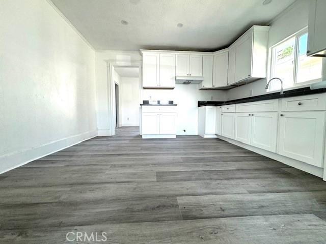 kitchen with dark countertops, wood finished floors, white cabinetry, and baseboards