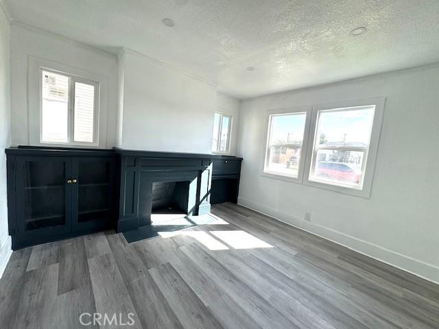 unfurnished living room with a fireplace with flush hearth, a textured ceiling, baseboards, and wood finished floors