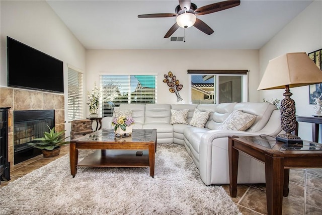 living room with a tiled fireplace, visible vents, and a ceiling fan