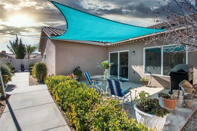 rear view of house with a patio area, fence, and stucco siding