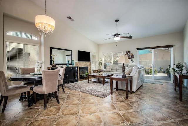 living room featuring high vaulted ceiling, visible vents, a tiled fireplace, and ceiling fan with notable chandelier