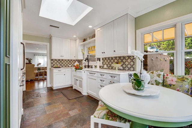 kitchen featuring white cabinets, a skylight, white fridge, backsplash, and crown molding