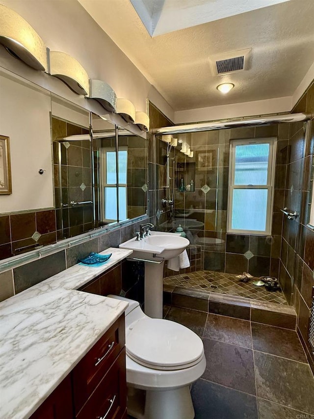 bathroom featuring toilet, tile walls, walk in shower, a textured ceiling, and sink