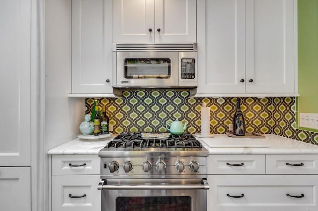 kitchen featuring stainless steel appliances, decorative backsplash, white cabinets, and light stone countertops