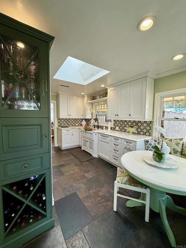 kitchen featuring tasteful backsplash, a skylight, sink, and white cabinetry