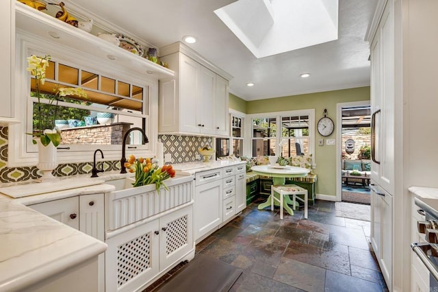 kitchen featuring a skylight, decorative backsplash, light stone counters, and white cabinetry