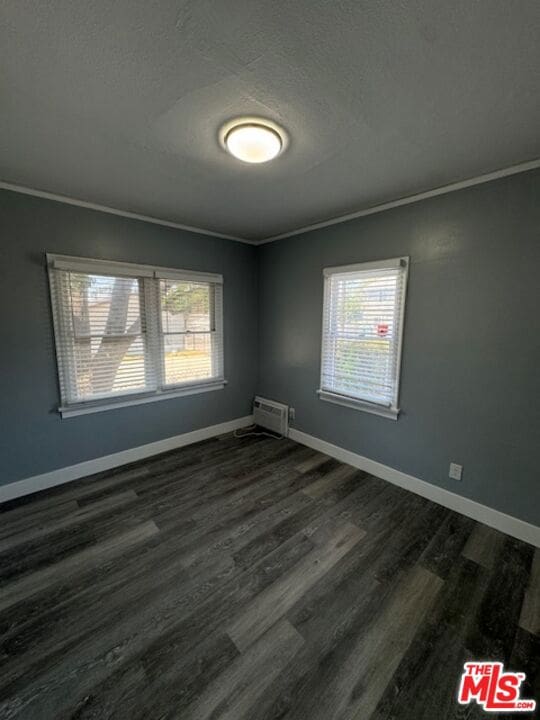 unfurnished room with crown molding, plenty of natural light, and dark wood-type flooring