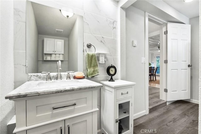 bathroom with wood finished floors, vanity, ceiling fan, baseboards, and visible vents