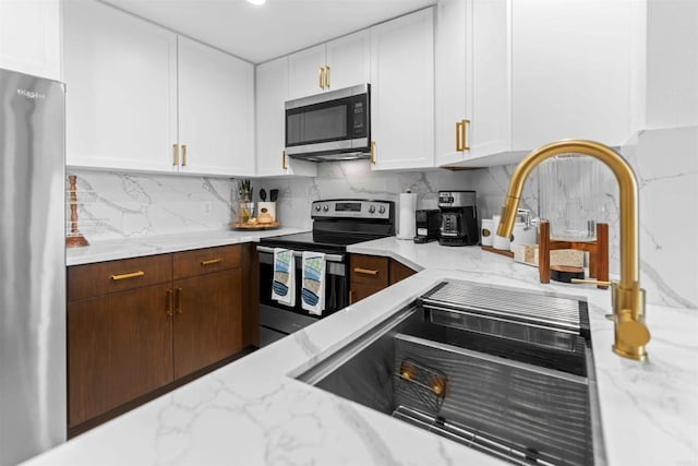 kitchen featuring backsplash, light stone counters, white cabinetry, and stainless steel appliances