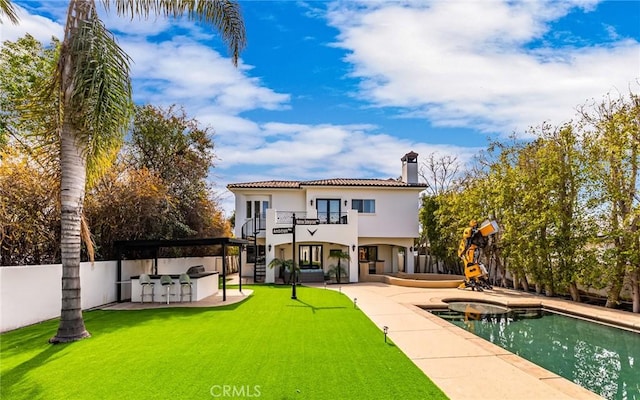 back of house featuring a balcony, an outdoor kitchen, a fenced in pool, a patio, and a yard