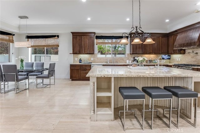 kitchen with tasteful backsplash, a spacious island, hanging light fixtures, light stone countertops, and a breakfast bar area