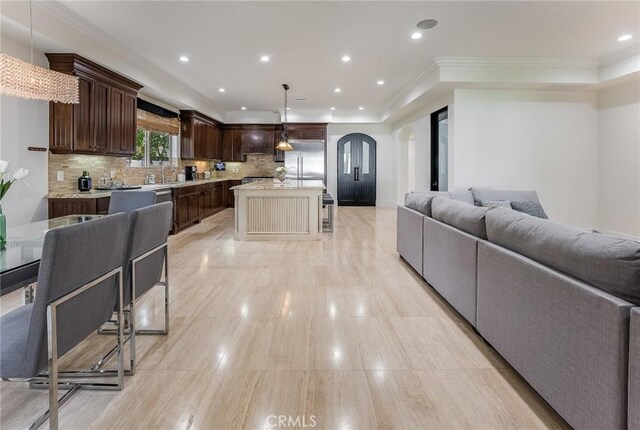 kitchen featuring backsplash, a kitchen island, hanging light fixtures, appliances with stainless steel finishes, and custom range hood