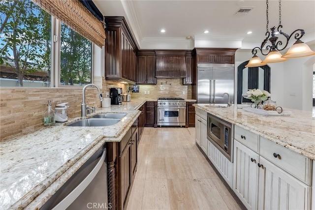 kitchen featuring white cabinets, custom exhaust hood, built in appliances, sink, and hanging light fixtures