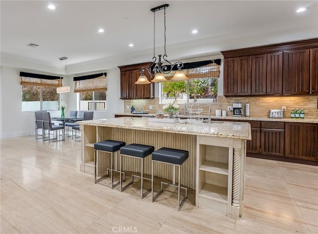 kitchen with a kitchen island, tasteful backsplash, hanging light fixtures, light stone counters, and crown molding