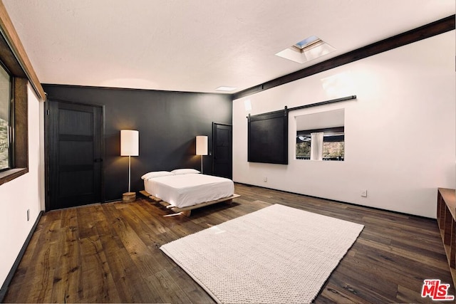 bedroom featuring a barn door, a skylight, and dark hardwood / wood-style floors