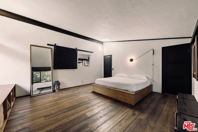 bedroom featuring a barn door, dark hardwood / wood-style floors, and a textured ceiling