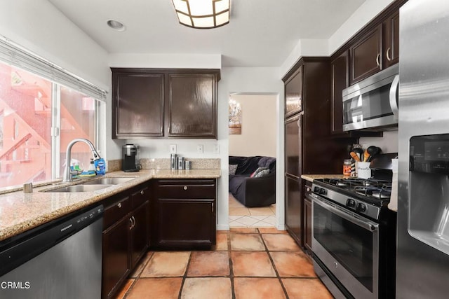 kitchen featuring dark brown cabinetry, light stone countertops, sink, stainless steel appliances, and light tile patterned floors