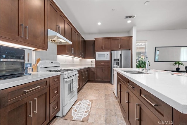 kitchen with white appliances, dark brown cabinetry, and sink