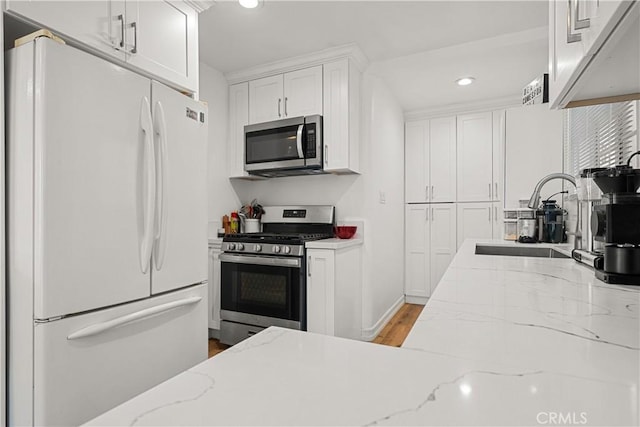 kitchen with sink, light stone countertops, light hardwood / wood-style floors, white cabinetry, and stainless steel appliances