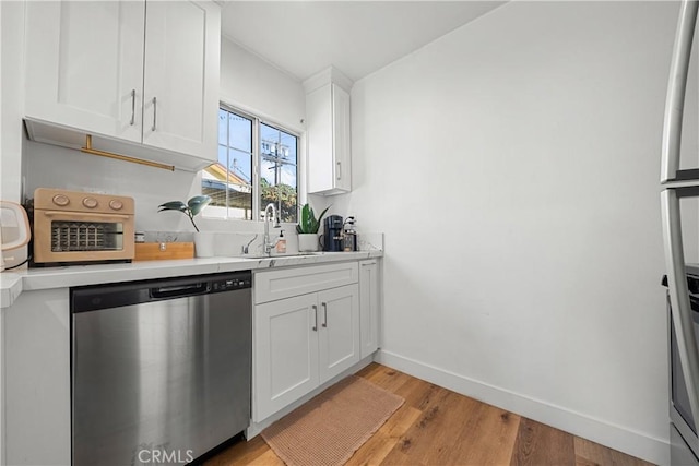 kitchen with white cabinets, light hardwood / wood-style flooring, stainless steel dishwasher, and sink