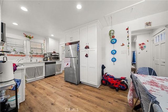 kitchen with decorative backsplash, stainless steel appliances, sink, light hardwood / wood-style floors, and white cabinetry