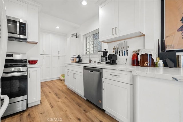 kitchen featuring light stone countertops, appliances with stainless steel finishes, sink, light hardwood / wood-style flooring, and white cabinetry