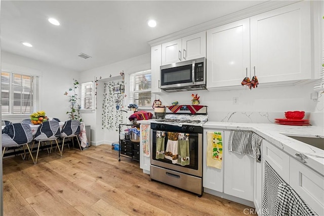 kitchen with white cabinets, light stone countertops, light wood-type flooring, and appliances with stainless steel finishes