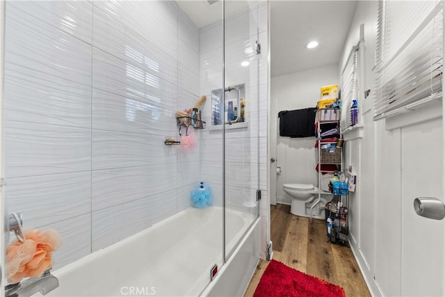 bathroom with combined bath / shower with glass door, hardwood / wood-style floors, and toilet