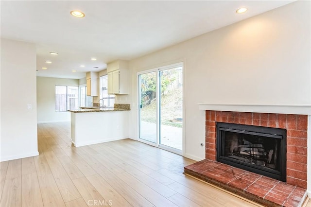 unfurnished living room featuring sink, light hardwood / wood-style floors, and a brick fireplace