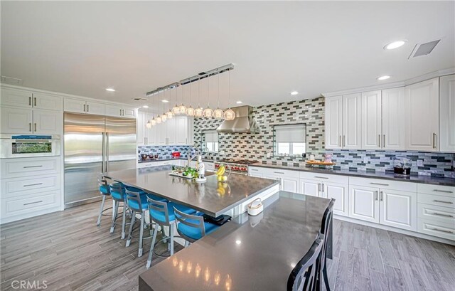 kitchen featuring premium appliances, light hardwood / wood-style floors, hanging light fixtures, and tasteful backsplash