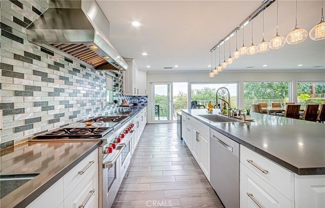 kitchen with sink, wall chimney exhaust hood, tasteful backsplash, decorative light fixtures, and appliances with stainless steel finishes