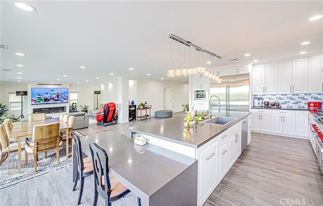 kitchen with stainless steel appliances, sink, decorative light fixtures, light hardwood / wood-style floors, and an island with sink