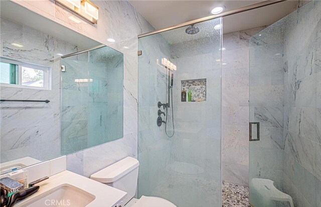 bathroom with vanity, a shower with door, toilet, and tile walls