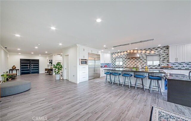 kitchen featuring a breakfast bar, decorative backsplash, light wood-type flooring, white cabinetry, and stainless steel appliances