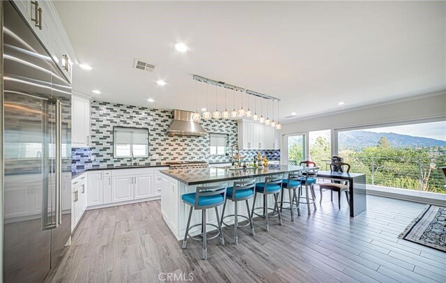 kitchen with tasteful backsplash, wall chimney range hood, decorative light fixtures, white cabinets, and built in fridge