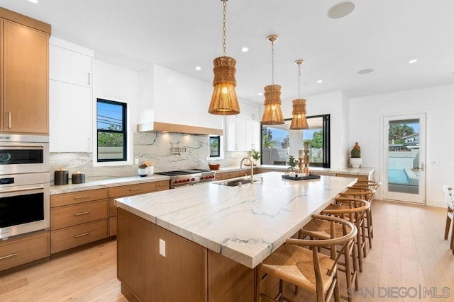 kitchen featuring a wealth of natural light, stainless steel appliances, pendant lighting, a kitchen island with sink, and white cabinets