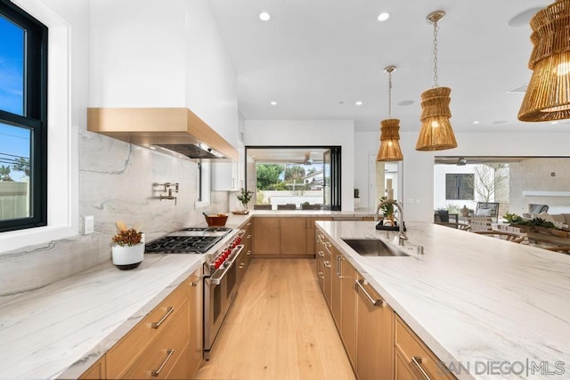 kitchen featuring pendant lighting, light stone counters, range with two ovens, and sink