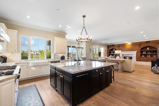 kitchen featuring decorative light fixtures, white cabinets, sink, and a center island with sink