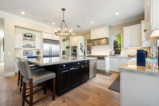 kitchen with light stone countertops, a kitchen island with sink, appliances with stainless steel finishes, and white cabinetry