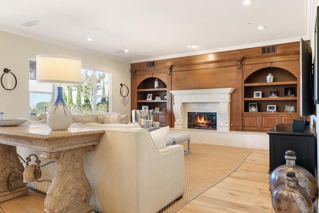 living room with built in features, ornamental molding, a premium fireplace, and light hardwood / wood-style flooring