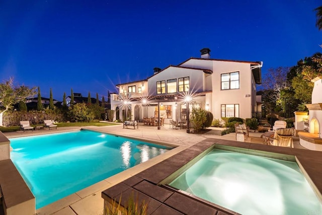 back house at twilight featuring a swimming pool with hot tub, an outdoor fireplace, and a patio area